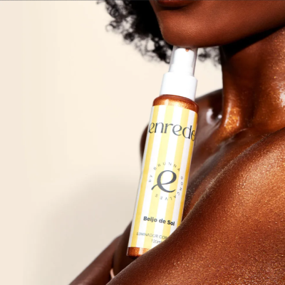 Frasco de spray corporal iluminador com design amarelo e branco na pele bronzeada