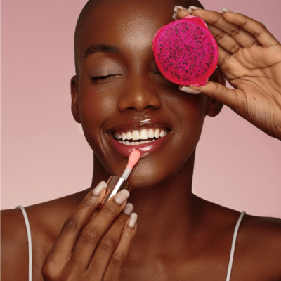 Pessoa com pele escura segurando pitaya rosa e aplicando batom cor-de-rosa