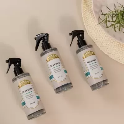 Três frascos de spray transparentes com rótulo branco, preto e dourado, ao lado de prato branco e raminho verde.