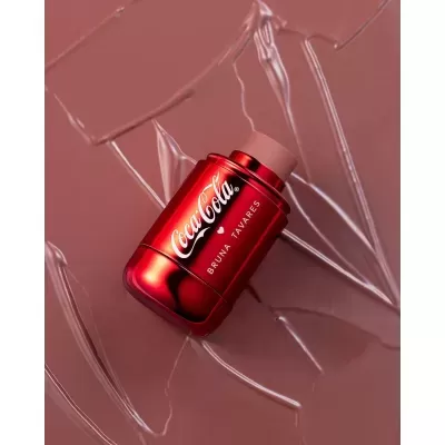 Stick de batom vermelho metálico Coca-Cola Bruna Tavares sobre fundo castanho texturizado
