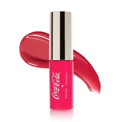 Batom líquido cor-de-rosa com tampa prateada e mancha de batom vermelho ao fundo