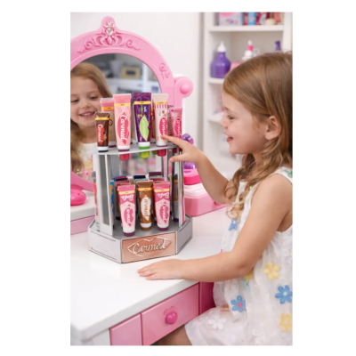 Menina loira a brincar com tubos de creme Carmel numa secretária com espelho rosa