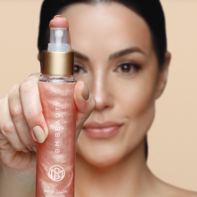 Frasco de spray BM BEAUTY com líquido rosa cintilante segurado por mulher