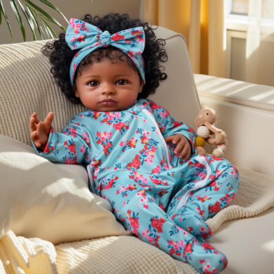 Boneca bebé com pijama azul claro estampado e faixa de cabelo sentada num sofá creme