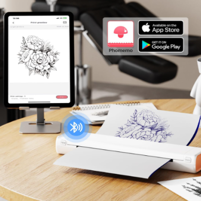 Impressora portátil branca a imprimir desenho floral azul em mesa com tablet a mostrar pré-visualização e ícones Phomemo, App Store e Google Play