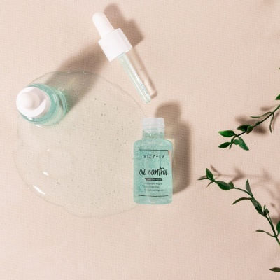 Frasco de sérum facial azul com conta-gotas sobre fundo claro e ramos verdes