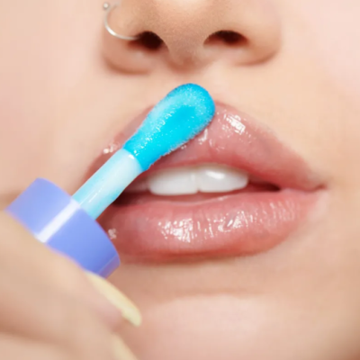 Aplicador de brilho labial azul e roxo a aplicar gloss transparente em lábios femininos