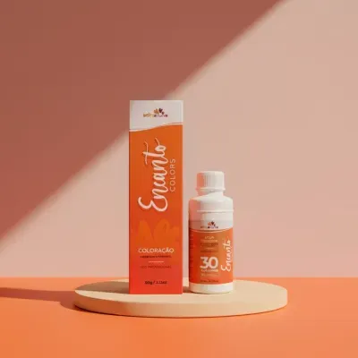 Embalagem e frasco branco de coloração capilar Encanto Colors em base clara sobre fundo laranja.