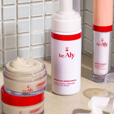 Produtos de cuidados faciais beAly com embalagens vermelhas, brancas e pêssego em superfície bege