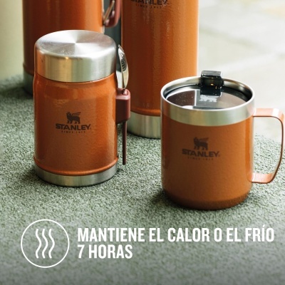 Utensílios térmicos Stanley laranja com tampa e colher sobre superfície verde.