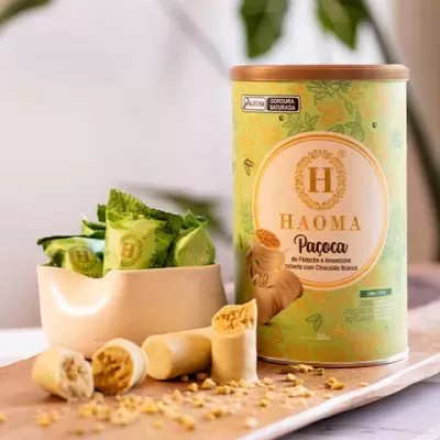 Lata verde HAOMA Paçoca pistache amendoim chocolate branco com embalagens individuais verdes e pedaços do doce numa tábua de madeira