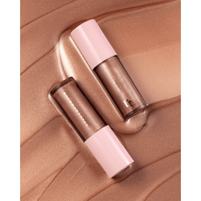 Dois batons líquidos bronze metálicos com tampa rosa claro sobre fundo bronze texturizado.