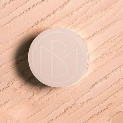 Pó compacto bege em embalagem redonda com logótipo em relevo sobre textura de pó