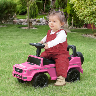 Criança num carro elétrico de brincar cor-de-rosa Mercedes no jardim