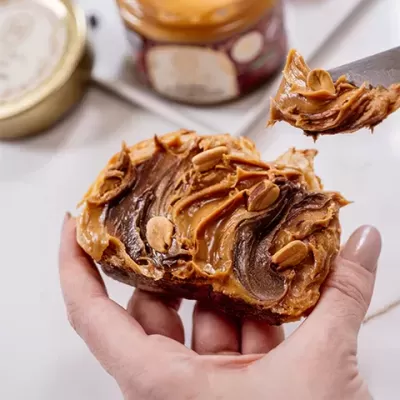 Torrada com creme de amendoim e pedaços de amendoim com colher a espalhar creme.