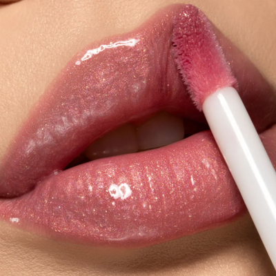 Lábios com brilho labial rosa dourado e aplicador branco