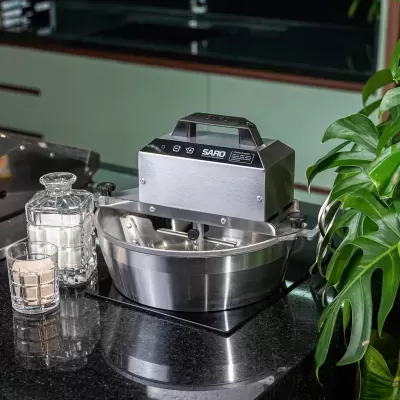 Batedeira profissional SARO de aço inoxidável numa bancada preta com frascos de vidro e planta verde