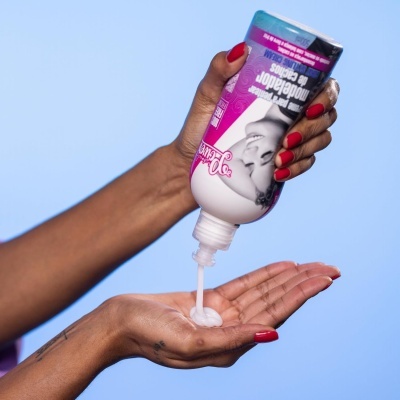 Mãos a despejar creme de frasco branco e roxo com texto em português