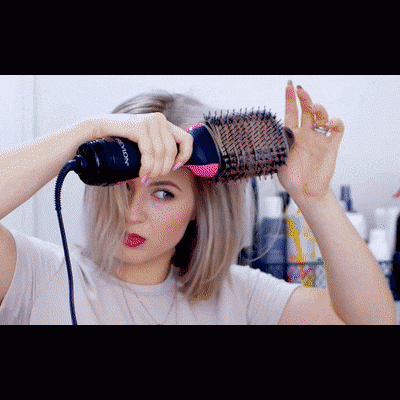 Mulher a usar escova rotativa elétrica preta e rosa para pentear cabelo em interior