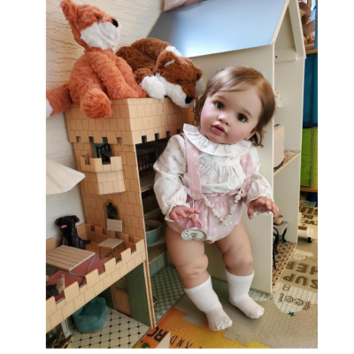 Boneca realista de bebé vestida de branco e rosa junto a castelo de madeira e peluches de raposas