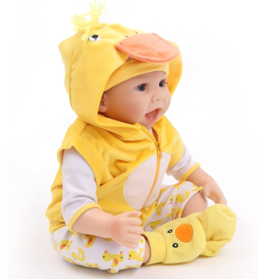 Boneca bebé com roupa de pato amarela e branca, capuz com bico e olhos, sentada sobre fundo branco.
