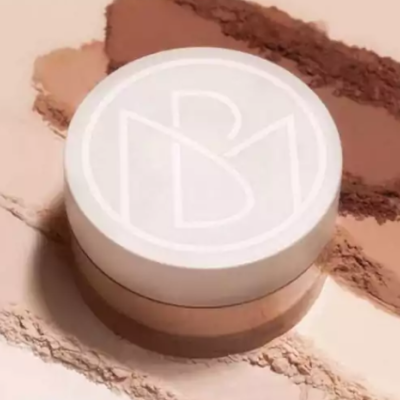 Pote branco de pó compacto com logo RBM sobre fundo com amostras de pós em tons castanhos e bege