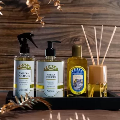 Conjunto de produtos Coala Ameixa Dourada e difusor de varetas sobre bandeja preta com fundo de madeira