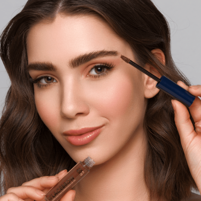 Mulher a aplicar máscara para sobrancelhas castanha com frasco transparente e tampa azul-escura