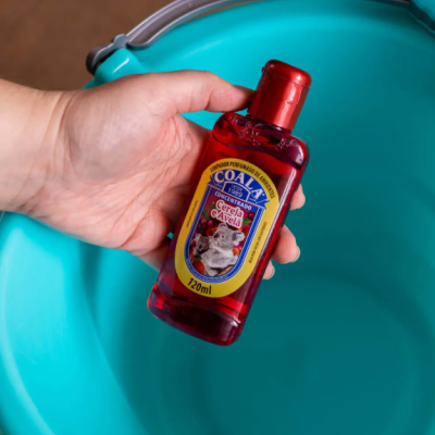 Frasco vermelho de concentrado perfumado COALA segurado sobre recipiente azul