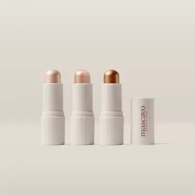 Três sticks de maquilhagem em tons perolados e embalagem branca com tampa ao lado