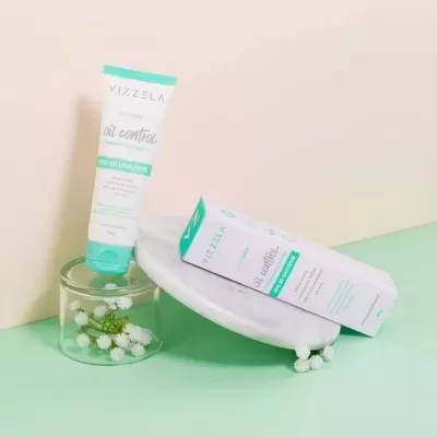 Tubo e embalagem do creme Vizzela Oil Control com flores brancas em frasco de vidro
