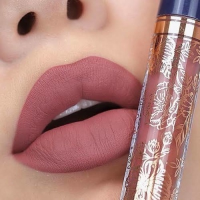 Lábios pintados com batom rosa antigo junto a tubo de batom líquido decorado