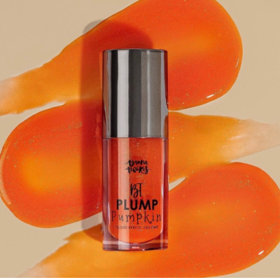 Frasco pequeno de gloss labial laranja com tampa preta sobre manchas alaranjadas.