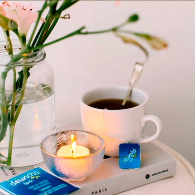 Vaso com flores, vela acesa, chávena branca com chá e pacote azul sobre livro 'PARIS'.