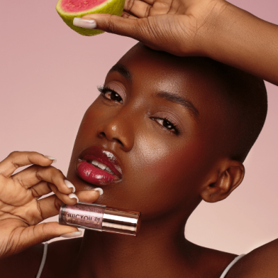 Mulher a segurar gloss labial e metade de goiaba com fundo rosa