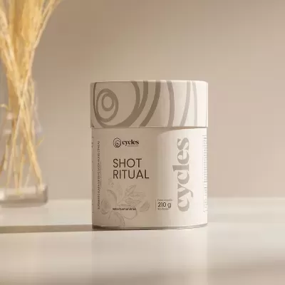 Embalagem creme do produto Shot Ritual com texto visível e vaso com palha seca ao lado.