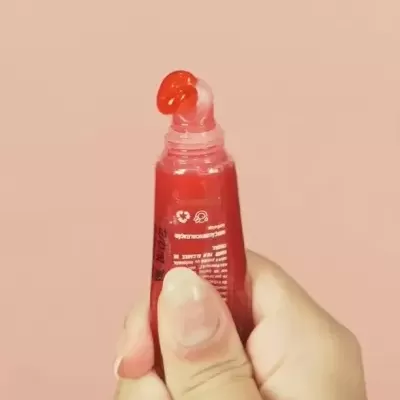 Tubo vermelho com gel vermelho e texto branco segurado por uma mão em fundo rosa