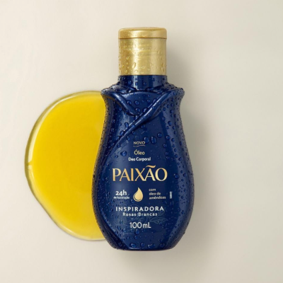 Frasco azul escuro com tampa dourada de óleo corporal PAIXÃO com óleo amarelo ao lado