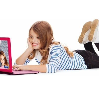 Menina deitada no chão a usar portátil rosa com imagem Barbie.