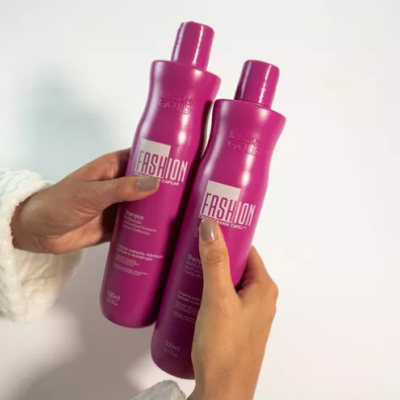 Duas garrafas cor-de-rosa FASHION CAPILAR seguradas por mãos.