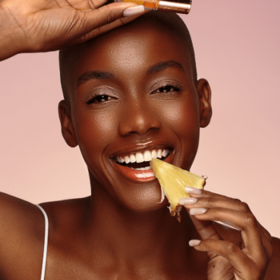 Mulher a sorrir com um frasco dourado e uma fatia de ananás