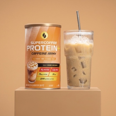 Embalagem de suplemento em pó Supercoffee Protein+ Caramel Macchiato ao lado de copo de vidro com bebida cremosa de gelo e canudo de metal