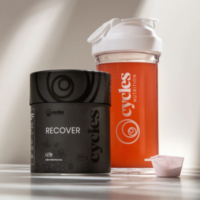 Suplemento alimentar RECOVER Cycles Nutrition em frasco preto com copo misturador e colher de dose.
