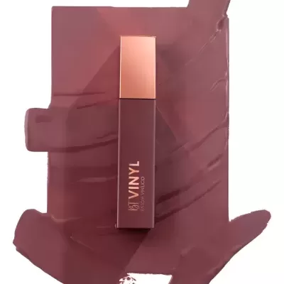 Gloss labial líquido castanho com embalagem retangular e tampa dourada sobre batom espalhado.