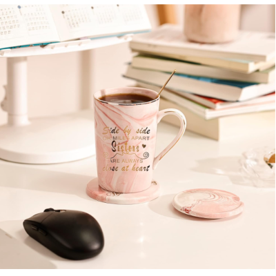 Caneca rosa com texto dourado e pires na mesa junto a rato e livros