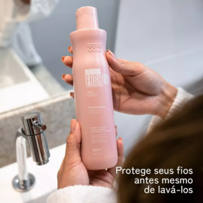 Frasco rosa de pré-shampoo Fashion Gold segurado por pessoa frente a pia com torneira metálica