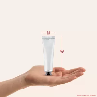 Tubo prateado pequeno medindo 10,6 cm x 2,5 cm em mão sobre fundo bege claro