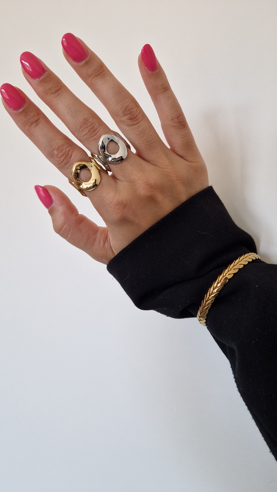 Mão com unhas rosas, anéis dourado e prateado e pulseira dourada