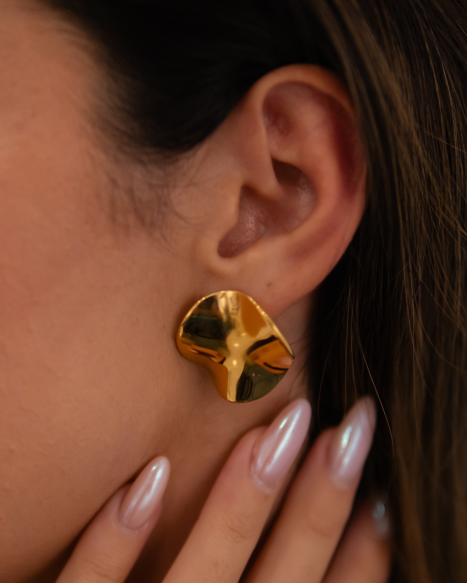 Brinco dourado com design irregular na orelha de uma pessoa