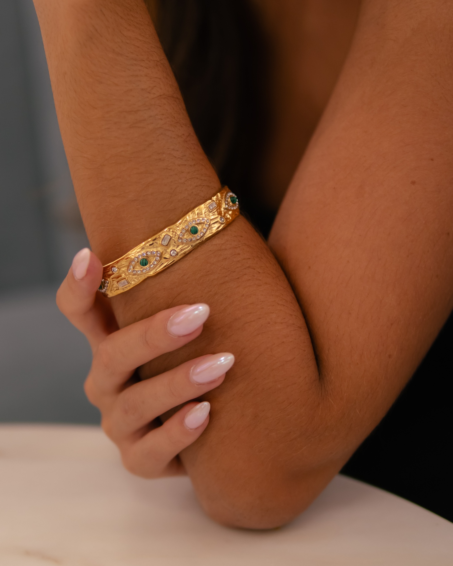 Pulseira dourada com pedras verdes e brancas no pulso de uma mulher